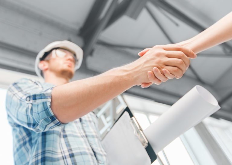trouver un architecte, Un ouvrier du bâtiment serrant la main d'un partenaire avec des plans d'architecte en main. Architecture et rénovation de maison