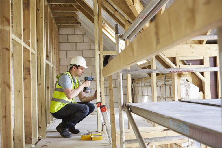 ouvrier du bâtiment utilisant une perceuse sur un chantier de construction d'une maison,