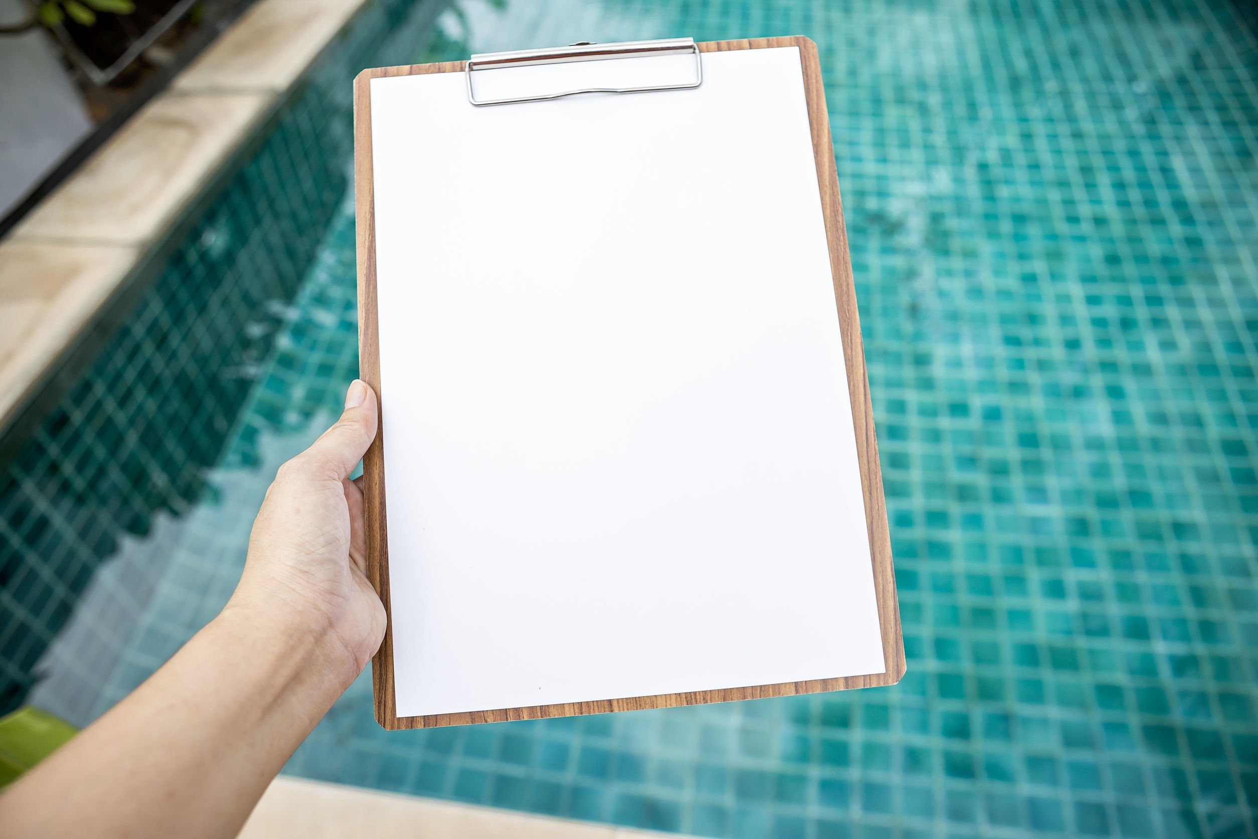une main tenant une feuille blanche au dessus d'une piscine, prix carrelage piscine