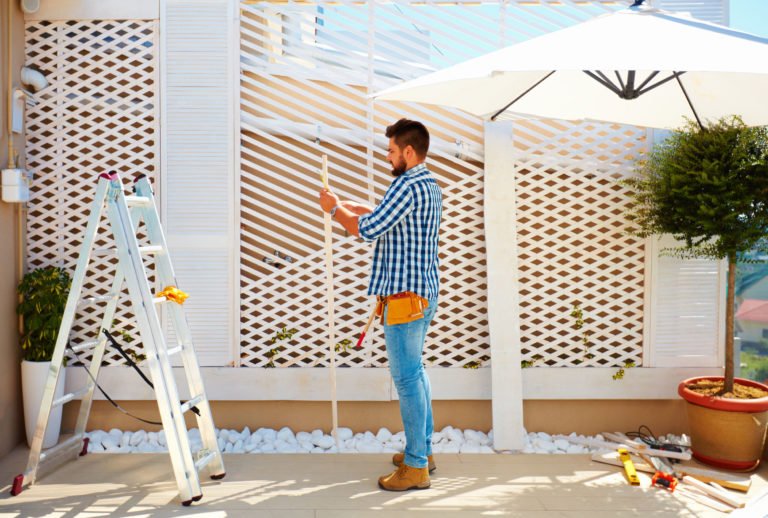 prix pergola bois, homme construisant une pergola en bois sur une terrasse au dessus d'une immeuble